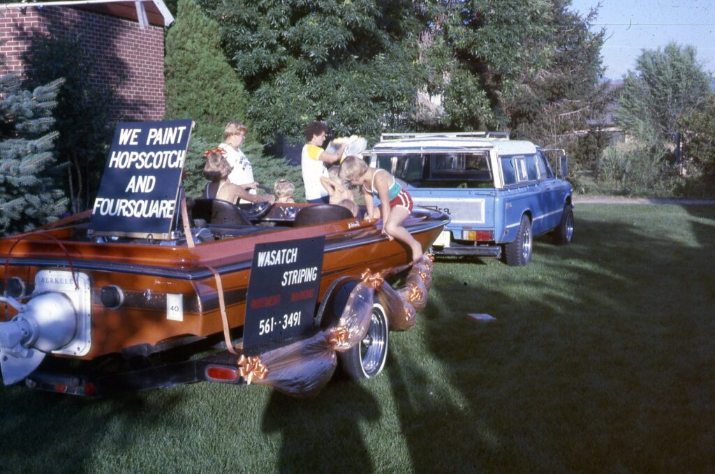 A truck pulling a boat with signs about Wasatch Striping, circa 1980's